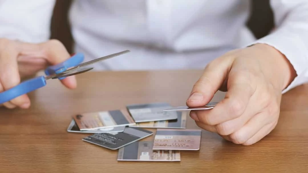 Hand cutting credit card with scissors on table 